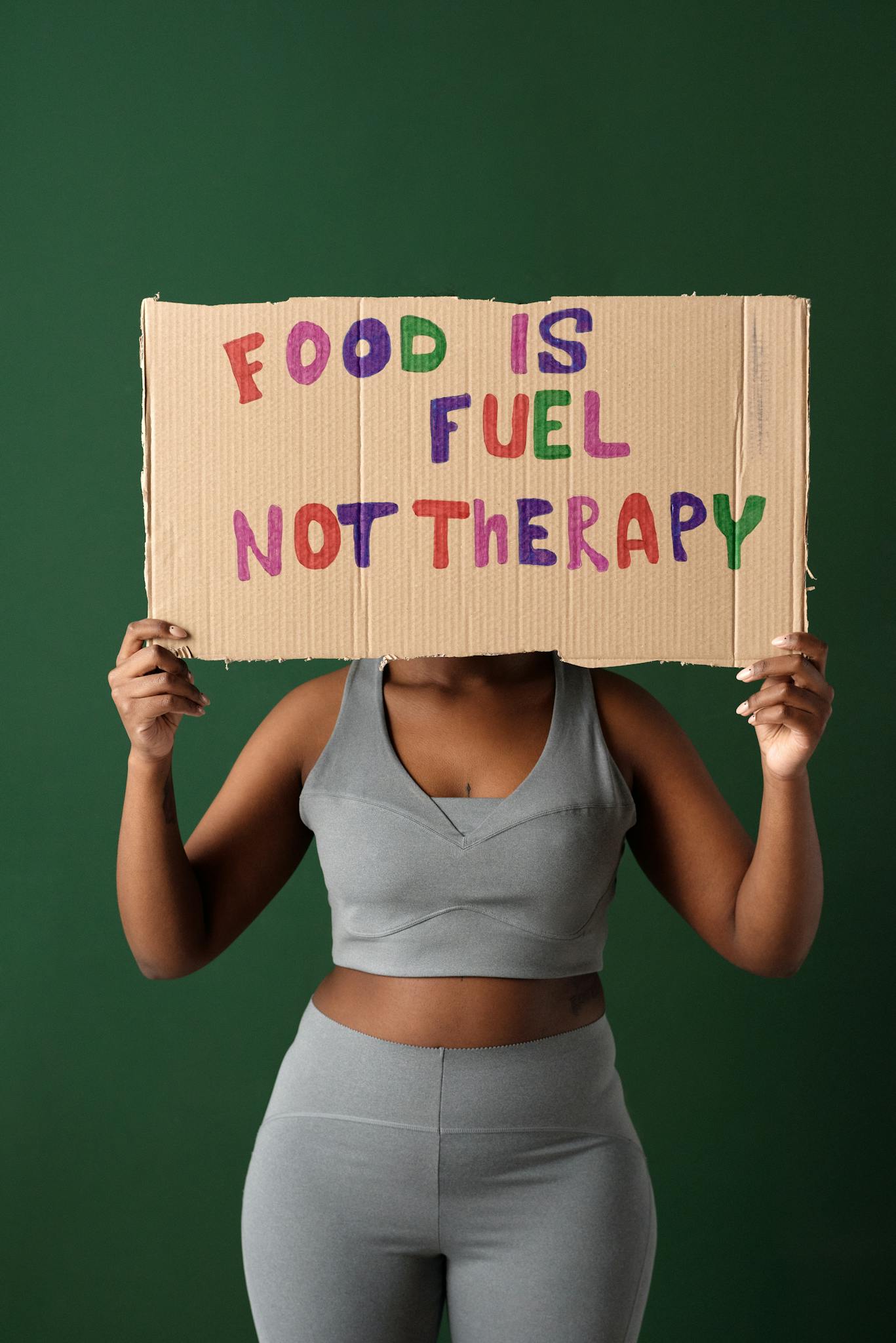 Woman holds sign reading 'Food is Fuel Not Therapy' promoting body positivity and a healthy lifestyle.
